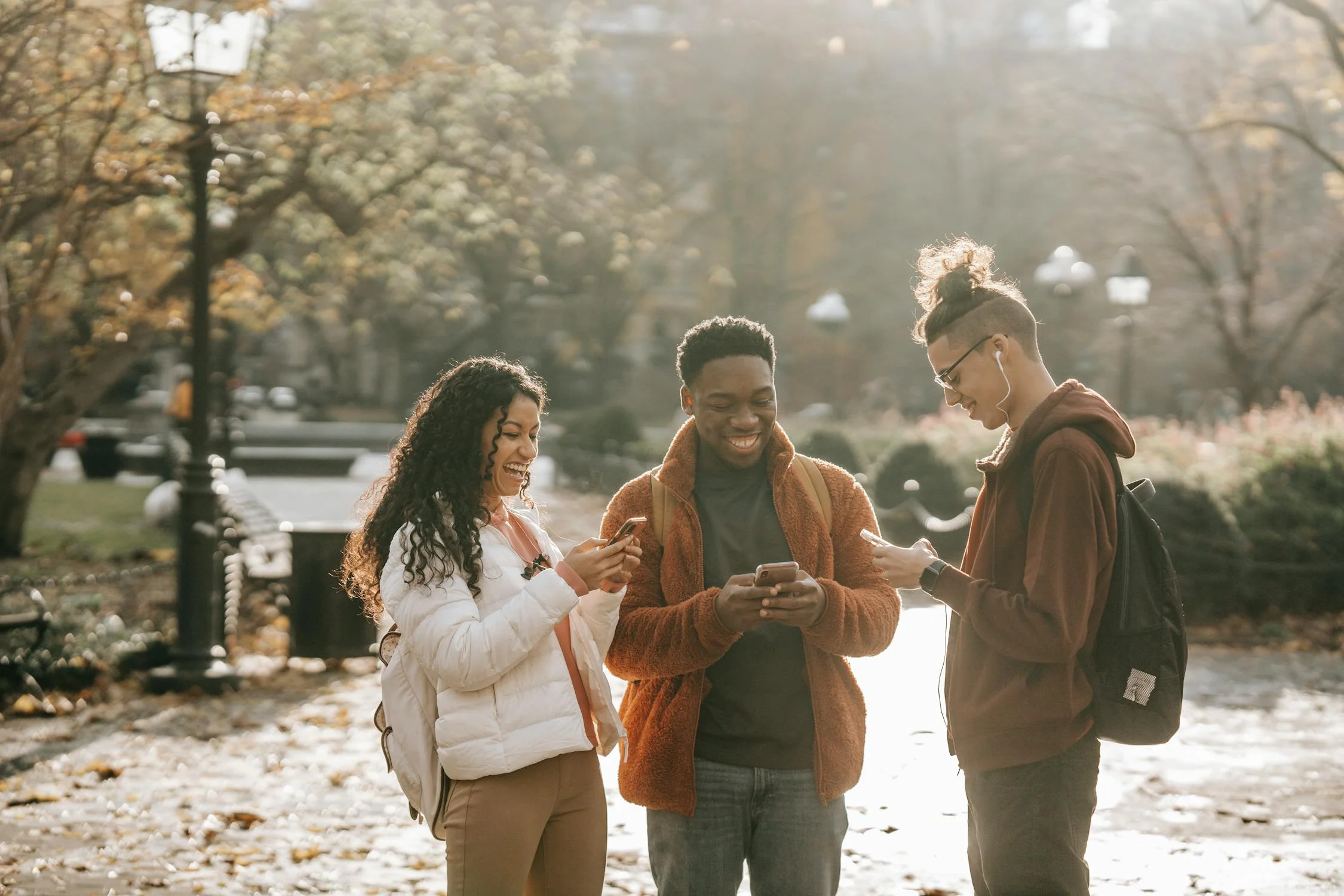 3 Students on their phones outside of a college campus