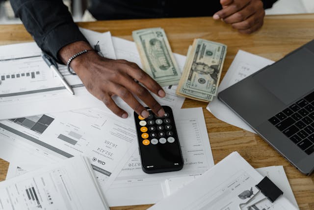 Person at table with bills, money, and is using their smartphone's calculator.